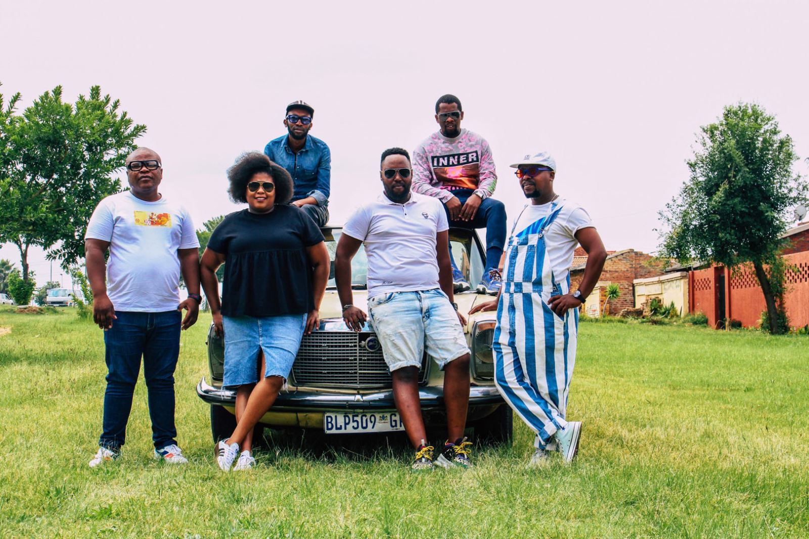 Group of peopl posing on a car in a field with lush green grass 